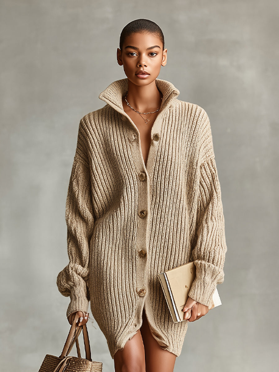 A woman wearing an oversized, beige ribbed-knit longline cardigan with a high funnel collar and button-up front, paired with tall brown leather boots.