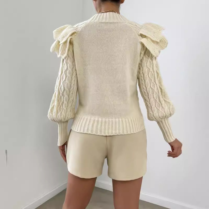 Off White - Women's cream chunky cable knit sweater featuring dramatic oversized ruffles on the shoulders and a ribbed crew neckline, styled with beige shorts and a brown belt.