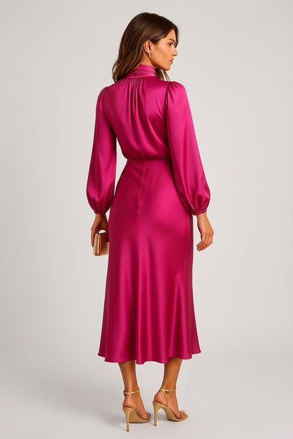 Hot Pink - A woman wearing a champagne-coloured satin midi dress with a high neckline, long balloon sleeves, and an elasticated waist, posing against a neutral grey background.