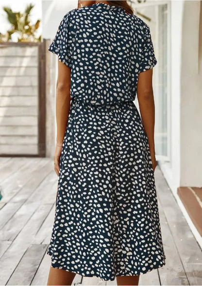 Deep Blue - Woman wearing a white midi shirt dress with a brown abstract spotted print, featuring a collared button-front bodice and a drawstring waist.