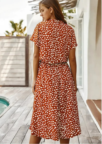 Light brown - Woman wearing a white midi shirt dress with a brown abstract spotted print, featuring a collared button-front bodice and a drawstring waist.