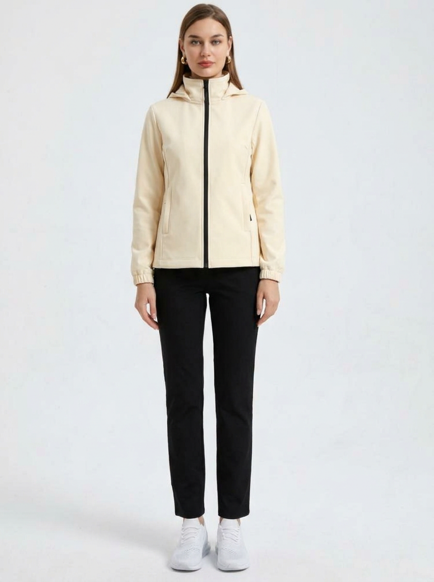 White - A woman wearing a cream-coloured structured hooded jacket with a contrast black front zipper, elasticised cuffs, and side pockets, paired with black pants.