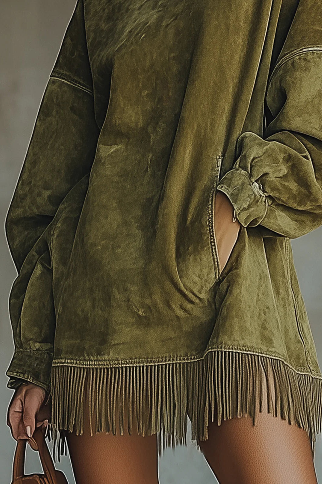 Model wearing a relaxed fit faux-suede mini dress featuring a high turtleneck, dropped long sleeves, front pockets, and a long fringe hemline.
