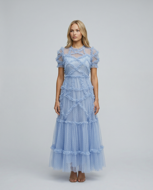Blue - A woman wearing a light blue Swiss dot tulle maxi dress with a high neck, tiered skirt, and ruffled chevron detailing.