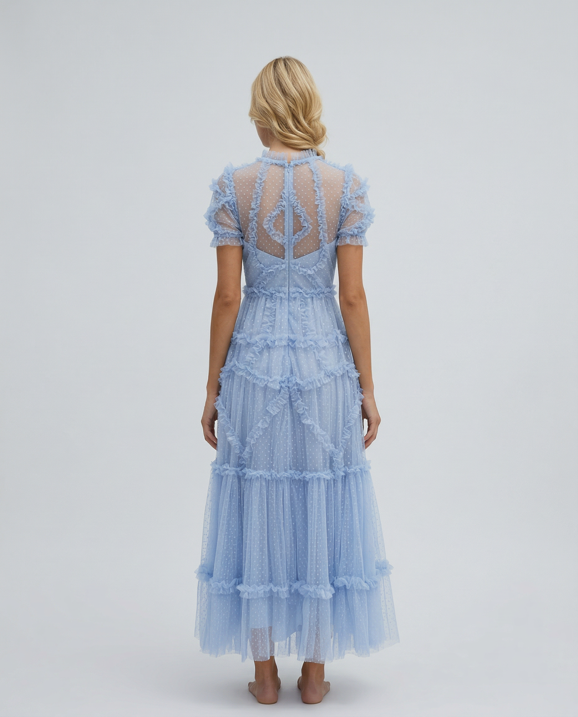 Blue - A woman wearing a light blue Swiss dot tulle maxi dress with a high neck, tiered skirt, and ruffled chevron detailing.