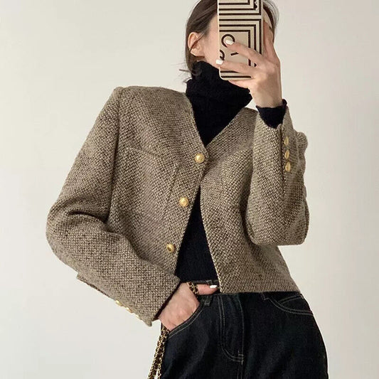 Brown - A woman wearing a tailored, cropped brown tweed jacket featuring a collarless V-neckline, front chest pockets, and gold-tone buttons, styled over a black turtleneck and dark denim.