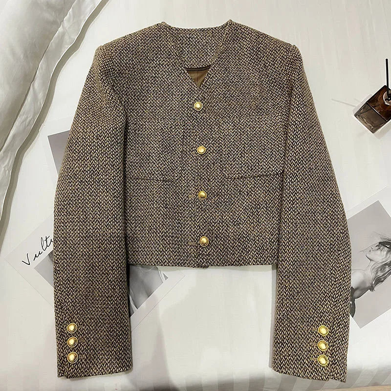 Brown - A woman wearing a tailored, cropped brown tweed jacket featuring a collarless V-neckline, front chest pockets, and gold-tone buttons, styled over a black turtleneck and dark denim.