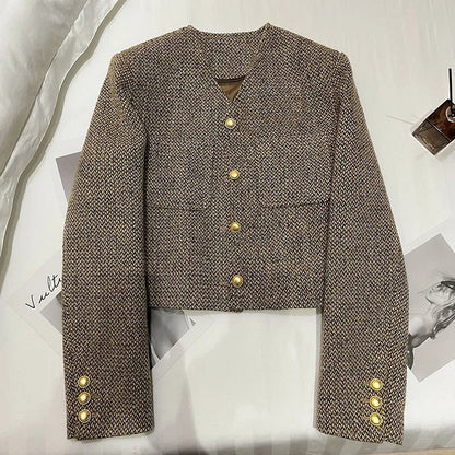 Brown - A woman wearing a tailored, cropped brown tweed jacket featuring a collarless V-neckline, front chest pockets, and gold-tone buttons, styled over a black turtleneck and dark denim.