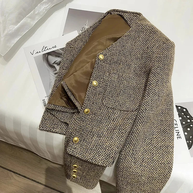Brown - A woman wearing a tailored, cropped brown tweed jacket featuring a collarless V-neckline, front chest pockets, and gold-tone buttons, styled over a black turtleneck and dark denim.