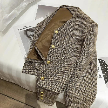 Brown - A woman wearing a tailored, cropped brown tweed jacket featuring a collarless V-neckline, front chest pockets, and gold-tone buttons, styled over a black turtleneck and dark denim.