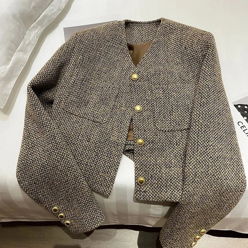 Brown - A woman wearing a tailored, cropped brown tweed jacket featuring a collarless V-neckline, front chest pockets, and gold-tone buttons, styled over a black turtleneck and dark denim.