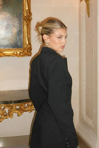 Black - Model standing on stairs wearing a tailored long-sleeve mini blazer dress with front buttons and flap pockets.