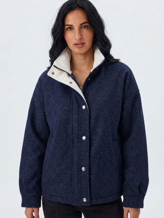 Navy - A woman wearing a dark navy blue textured jacket with a high stand collar lined in contrast cream fleece, featuring a snap-button front closure and a relaxed fit.