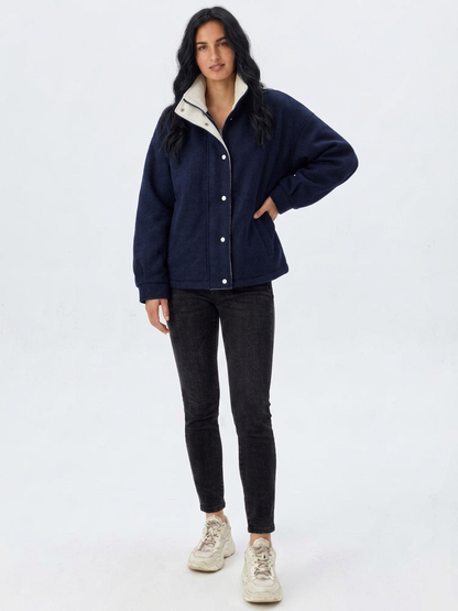 Navy - A woman wearing a dark navy blue textured jacket with a high stand collar lined in contrast cream fleece, featuring a snap-button front closure and a relaxed fit.