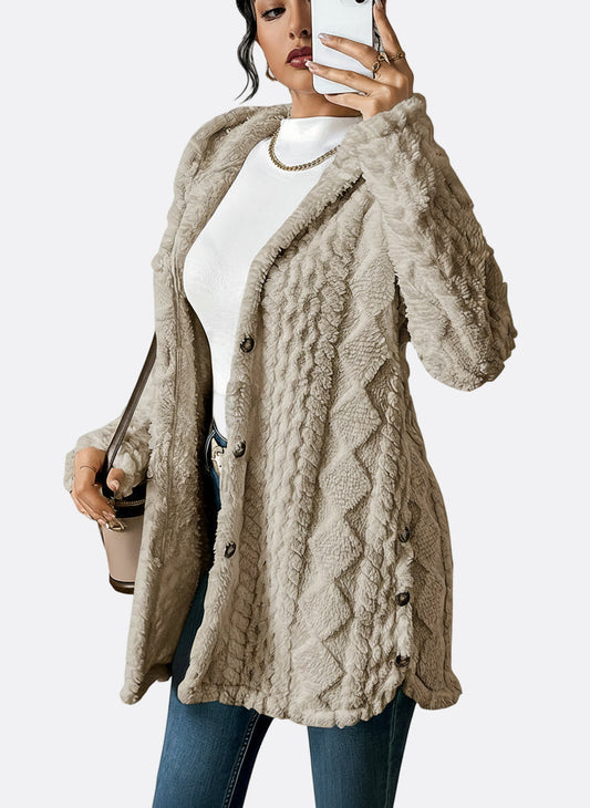 A woman wearing a beige, mid-length textured fleece hooded jacket with a diamond pattern, button closure, and buttoned side vents, layered over a white high-neck top and blue jeans.