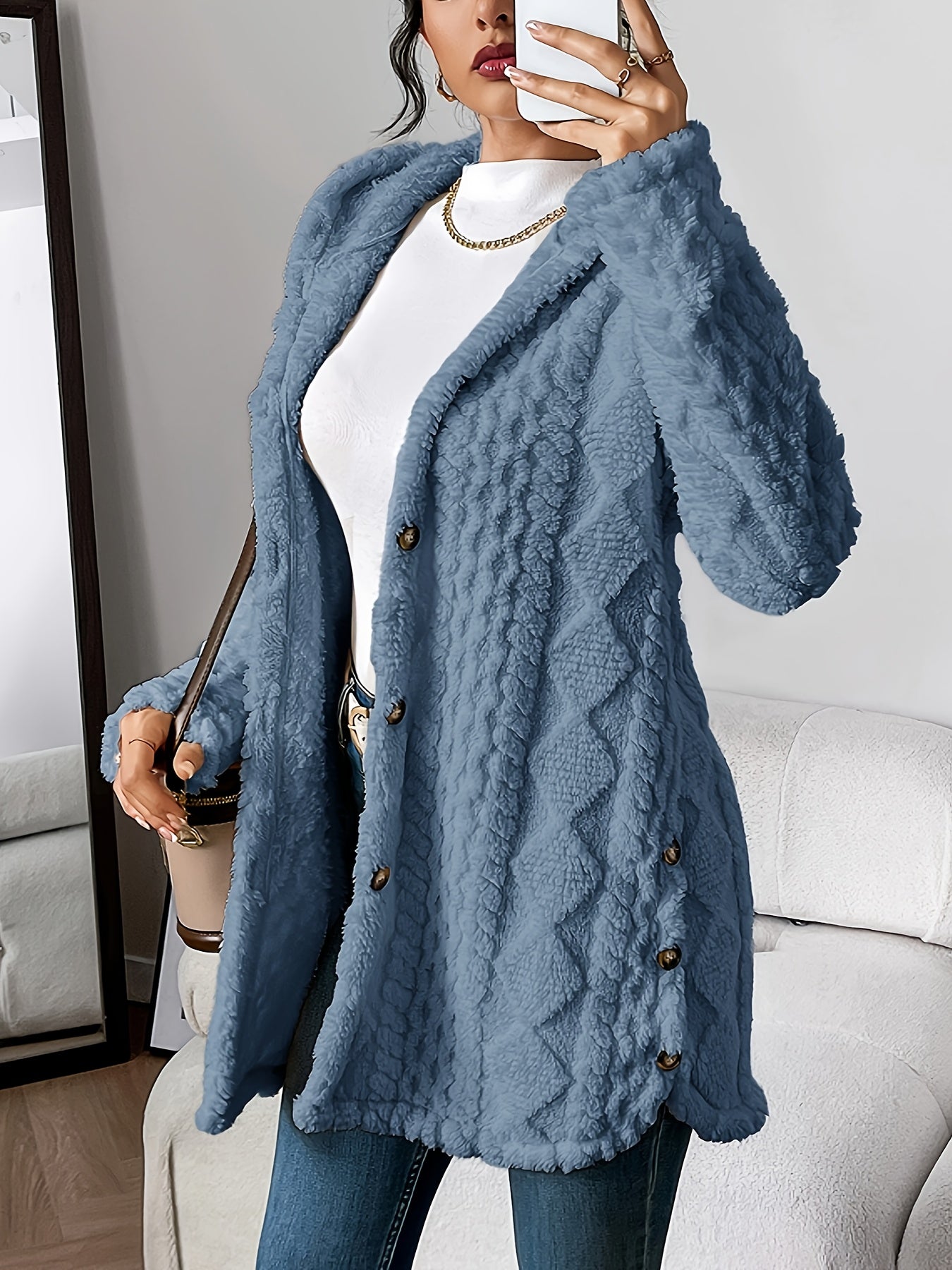 Denim Blue - A woman wearing a beige, mid-length textured fleece hooded jacket with a diamond pattern, button closure, and buttoned side vents, layered over a white high-neck top and blue jeans.