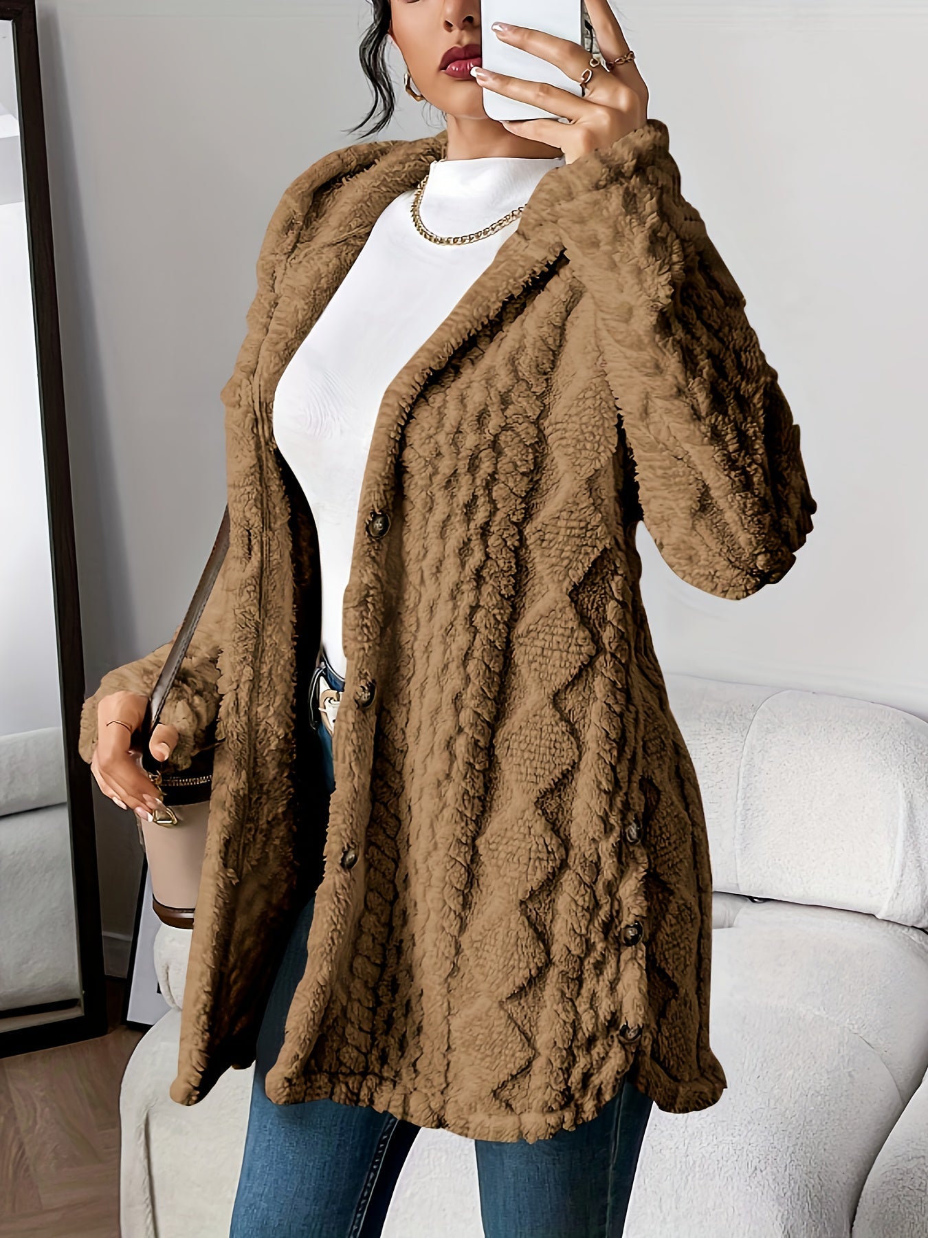 Black - A woman wearing a beige, mid-length textured fleece hooded jacket with a diamond pattern, button closure, and buttoned side vents, layered over a white high-neck top and blue jeans.