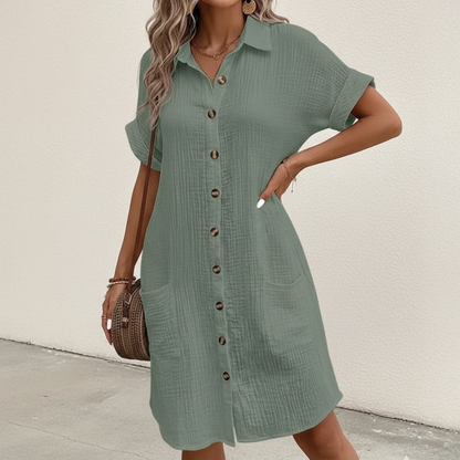 Green - A woman wearing a white, short-sleeved textured gauze shirt dress with a button-down front, collar, and two front patch pockets.
