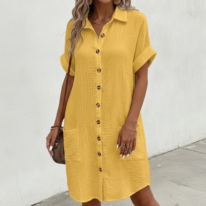 Yellow - A woman wearing a white, short-sleeved textured gauze shirt dress with a button-down front, collar, and two front patch pockets.
