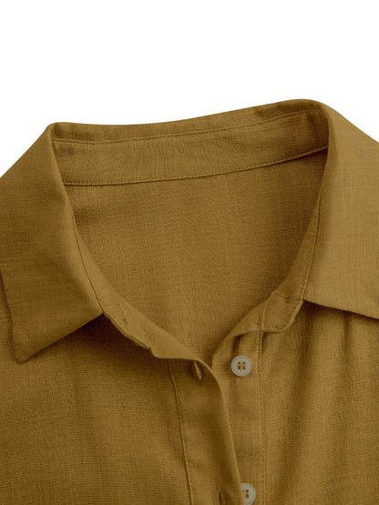 Mustard - A woman wearing a mustard-coloured, long-sleeve midi shirt dress made of a textured fabric. The dress features a pointed collar, button-down front, and a matching fabric tie belt at the waist.