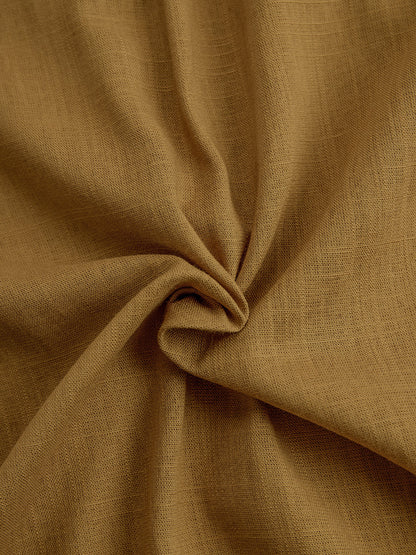 Mustard - A woman wearing a mustard-coloured, long-sleeve midi shirt dress made of a textured fabric. The dress features a pointed collar, button-down front, and a matching fabric tie belt at the waist.