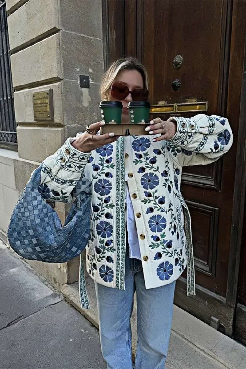 Blue - Women's cream mid-length jacket featuring blue and burgundy floral embroidery, a matching tie-waist belt, and button-front closure, styled over denim.