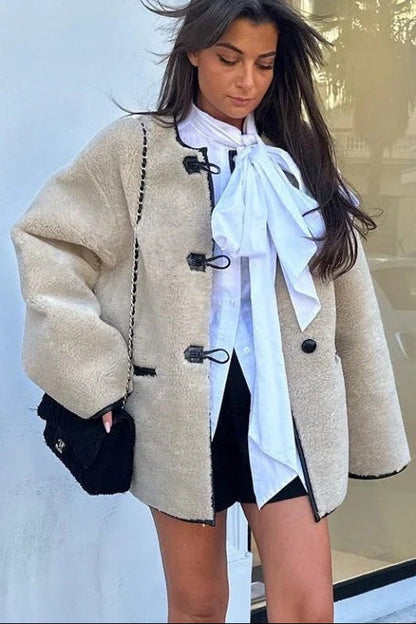 Women's heavyweight cream faux shearling jacket featuring a collarless neckline, black toggle closures, contrast black piping, and an oversized fit.