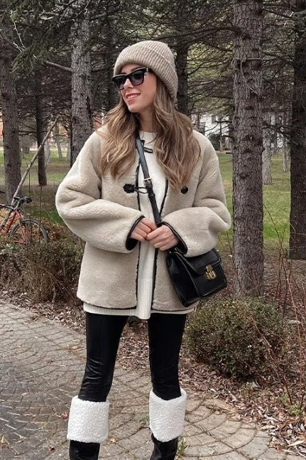 Women's heavyweight cream faux shearling jacket featuring a collarless neckline, black toggle closures, contrast black piping, and an oversized fit.