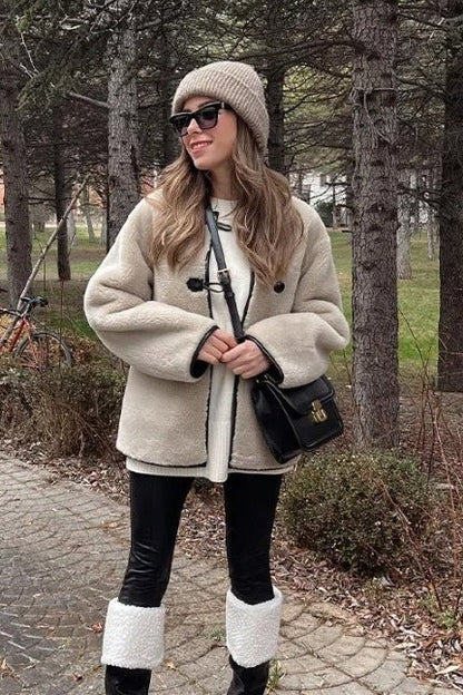 Women's heavyweight cream faux shearling jacket featuring a collarless neckline, black toggle closures, contrast black piping, and an oversized fit.