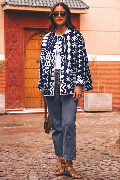 Dark Blue - Woman wearing a navy blue quilted open-front jacket with bold white abstract geometric embroidery, styled with jeans and sandals.