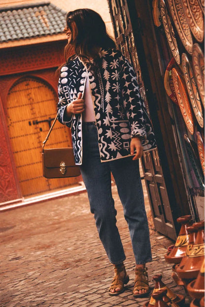 Dark Blue - Woman wearing a navy blue quilted open-front jacket with bold white abstract geometric embroidery, styled with jeans and sandals.