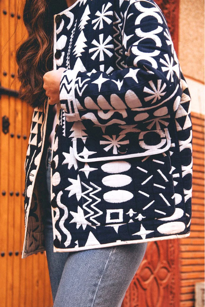 Dark Blue - Woman wearing a navy blue quilted open-front jacket with bold white abstract geometric embroidery, styled with jeans and sandals.